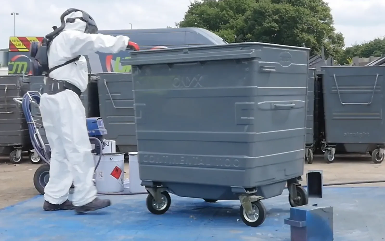 Worker applying cleaning solution to 1100L steel wheelie bin during on-site refurbishment process