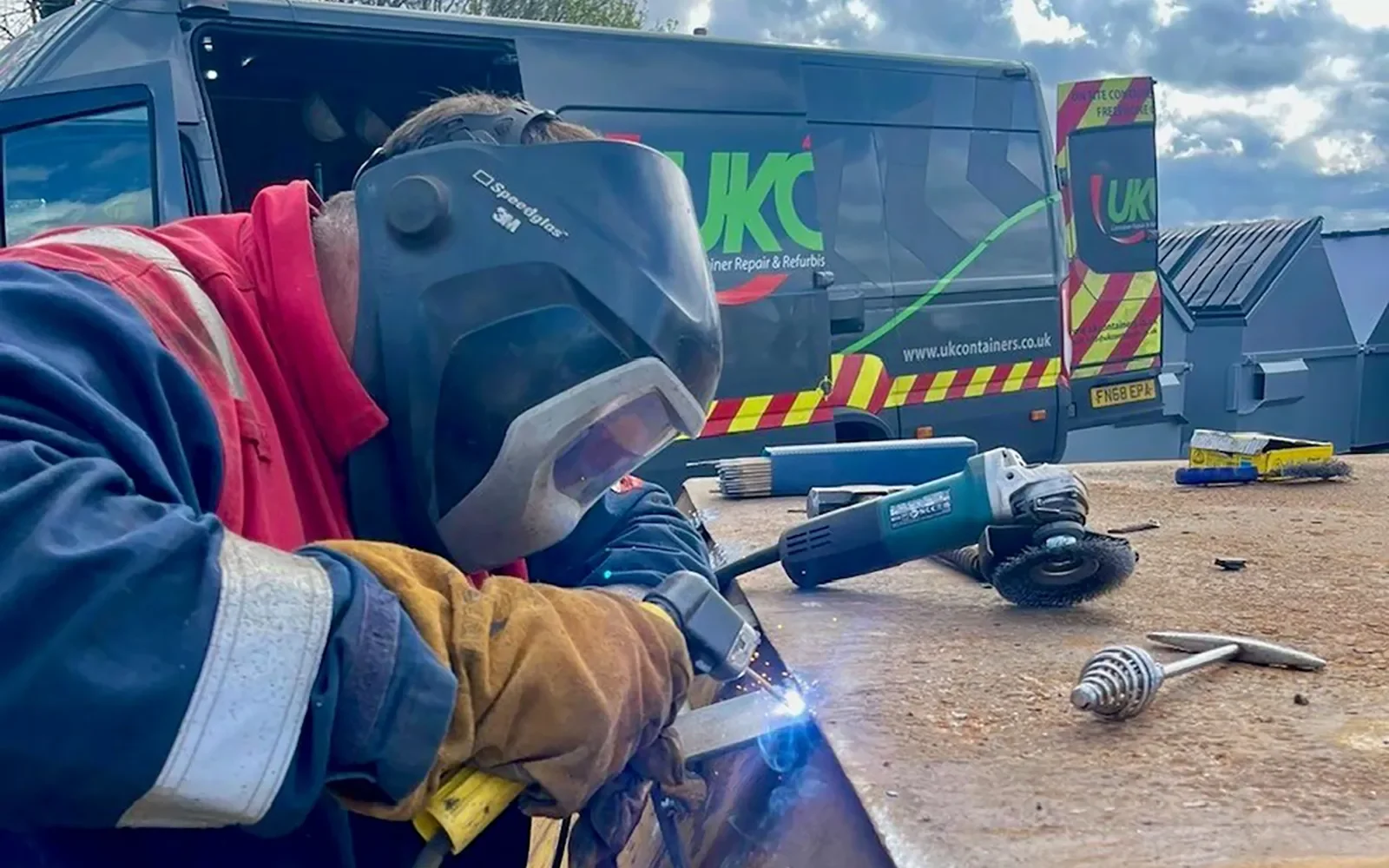 Worker welding and grinding a steel wheelie bin during on-site refurbishment